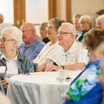 A woman and man are seated at a table with their attention directed to the front